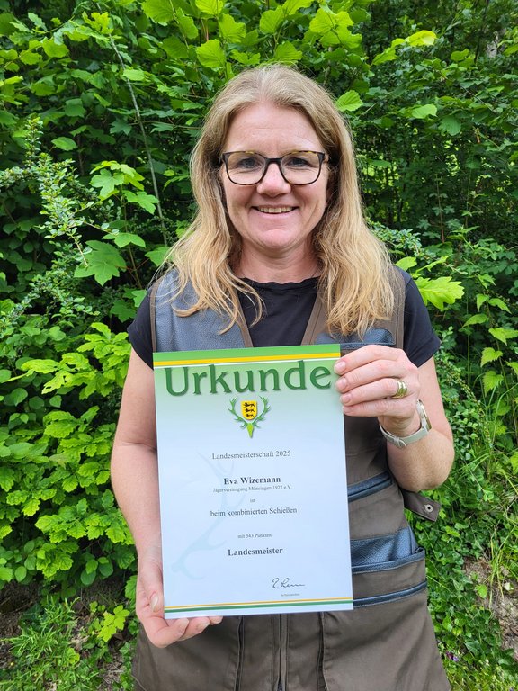Eine Frau hält eine Urkunde im Freien. Text auf der Urkunde: "Urkunde Landesmeisterschaft 2023 Eva Wiezmann Jagdgesellschaft Illingen 1923 e.V. beim kombinierten Schießen mit 345 Punkten Landesmeister."